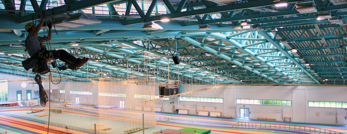 Höhenarbeiter wechselt das Leuchtmittel aus Strahler. Er hängt in einer Turnhalle von der Decke. Alles aus dem Seil mit Helm und ohne Steiger.