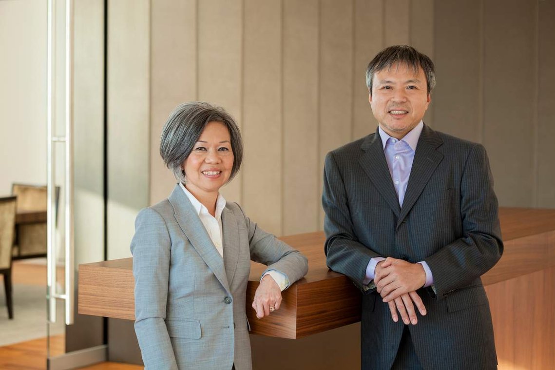 Formal group portrait of two CEOs in a modern room, leaning on a modern standing table.