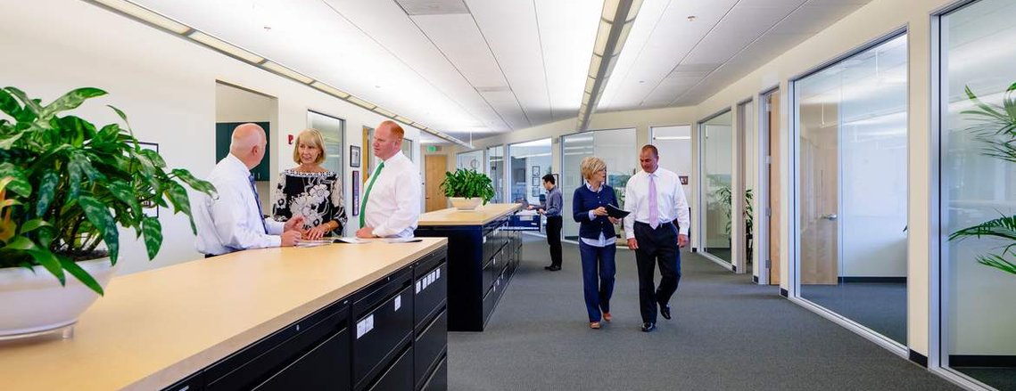 Wide photo of an office lifestyle image in an investment firm in Novato, California. There are three groups of people talking.