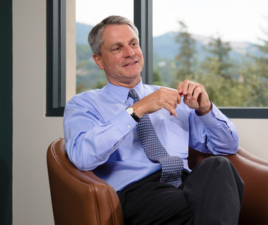 Office lifestyle portrait of an executive man in a meeting. Outside the office window is an out-of-focus city of Novato, California, trees, and other greenery.