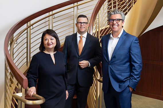 Formal 3-person team/group shot of wealth managers at a First Republic Bank in San Francisco, California. The team members are posed in front of a large, winding staircase.