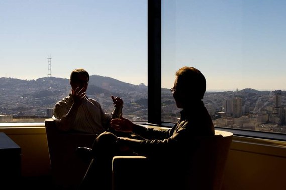 Window silhouette of two office workers talking with San Francisco and Twin Peaks in the background
