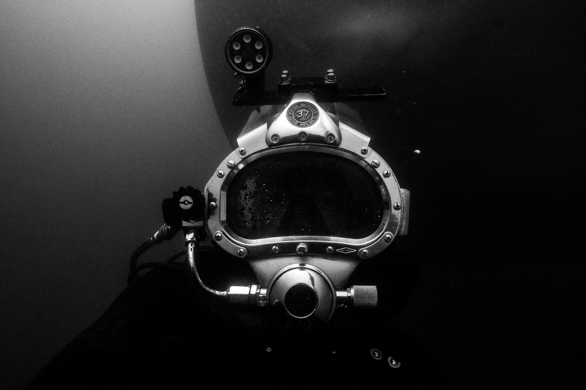 Deep sea diver in dive suite submerged underwater talking a self-portrait photograph.