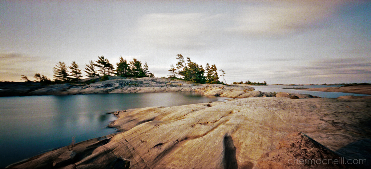 digital scan of a panoramic pinhole photo of a Georgian Bay landscape including rocky shores, trees and water taken at dawn (sunrise).