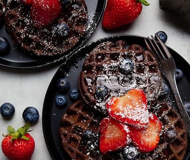 Chocolate Waffles topped with fresh strawberries and blueberries, covered with syrup and powder sugar.