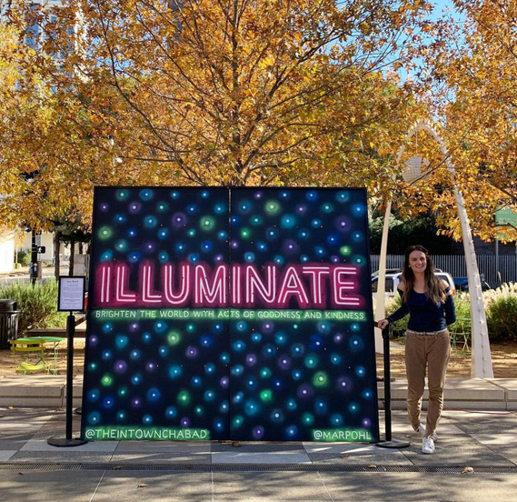 Marpohl stands next to Hanukkah mural with painted neon lights. The large word reads 