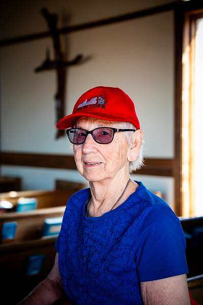 An elderly woman stands on the steps of a historic wooden church in Arizona, smiling under the blue sky. This travel and heritage photo combines senior lifestyle photography with cultural tourism, reflecting spiritual journeys and meaningful moments.