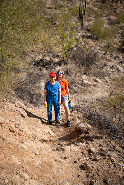 A fit 90-year-old woman walks a rugged desert trail in Arizona, showcasing her love for hiking and staying active. Surrounded by cacti and earthy terrain, this lifestyle photo captures senior adventure, healthy aging, and outdoor exploration in the Southw