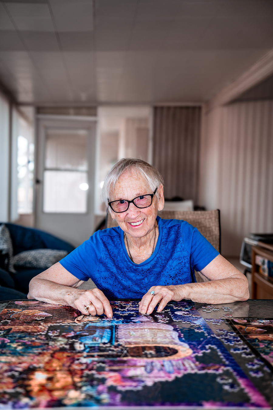 Captured in a cozy home setting, this vibrant senior enjoys solving a detailed jigsaw puzzle, embodying healthy lifestyle habits for aging adults.