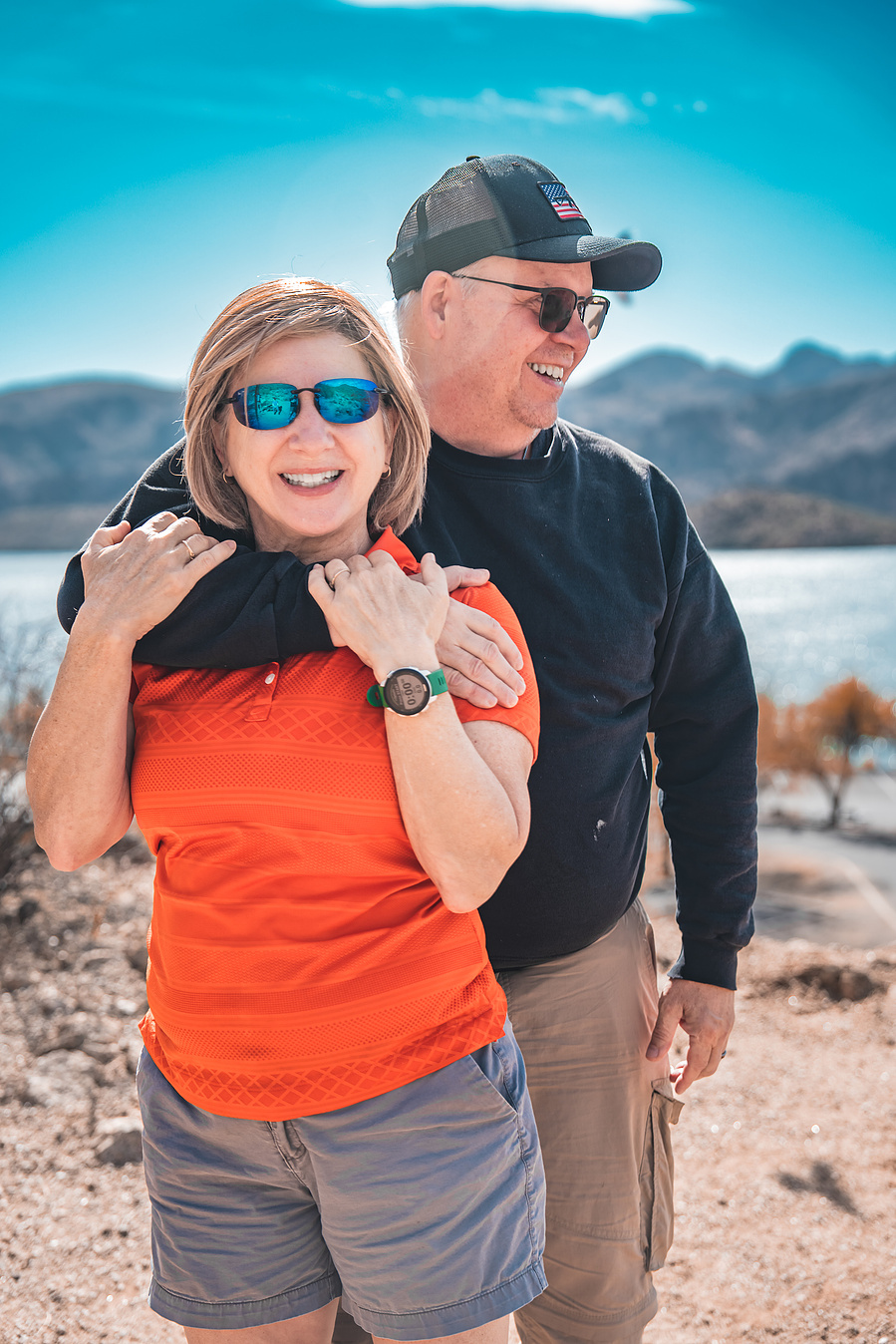 Romantic couple hugging on a trail overlooking Saguaro Lake, surrounded by wild desert landscape.