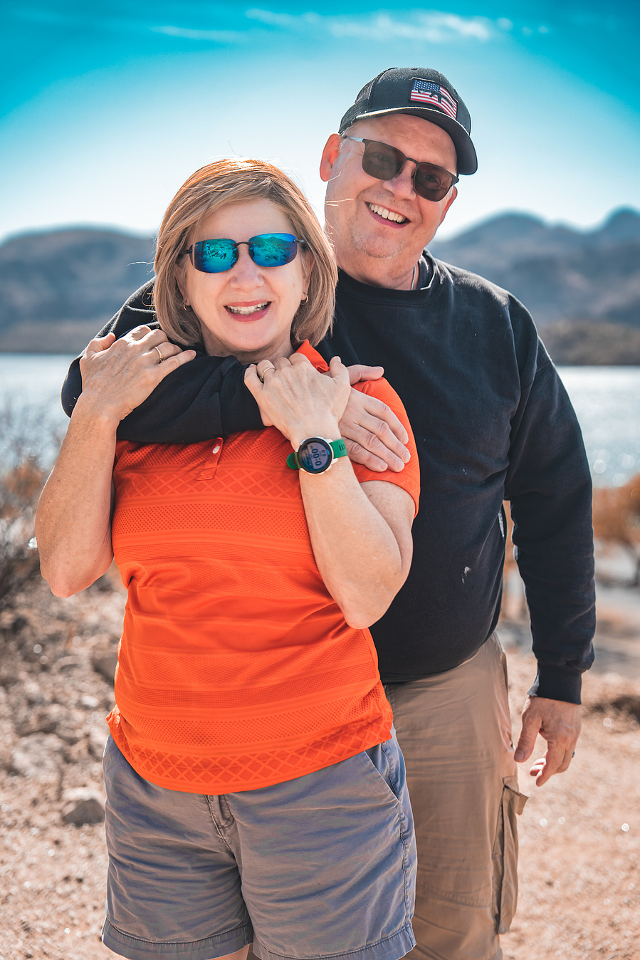 Romantic couple hugging on a trail overlooking Saguaro Lake, surrounded by wild desert landscape.