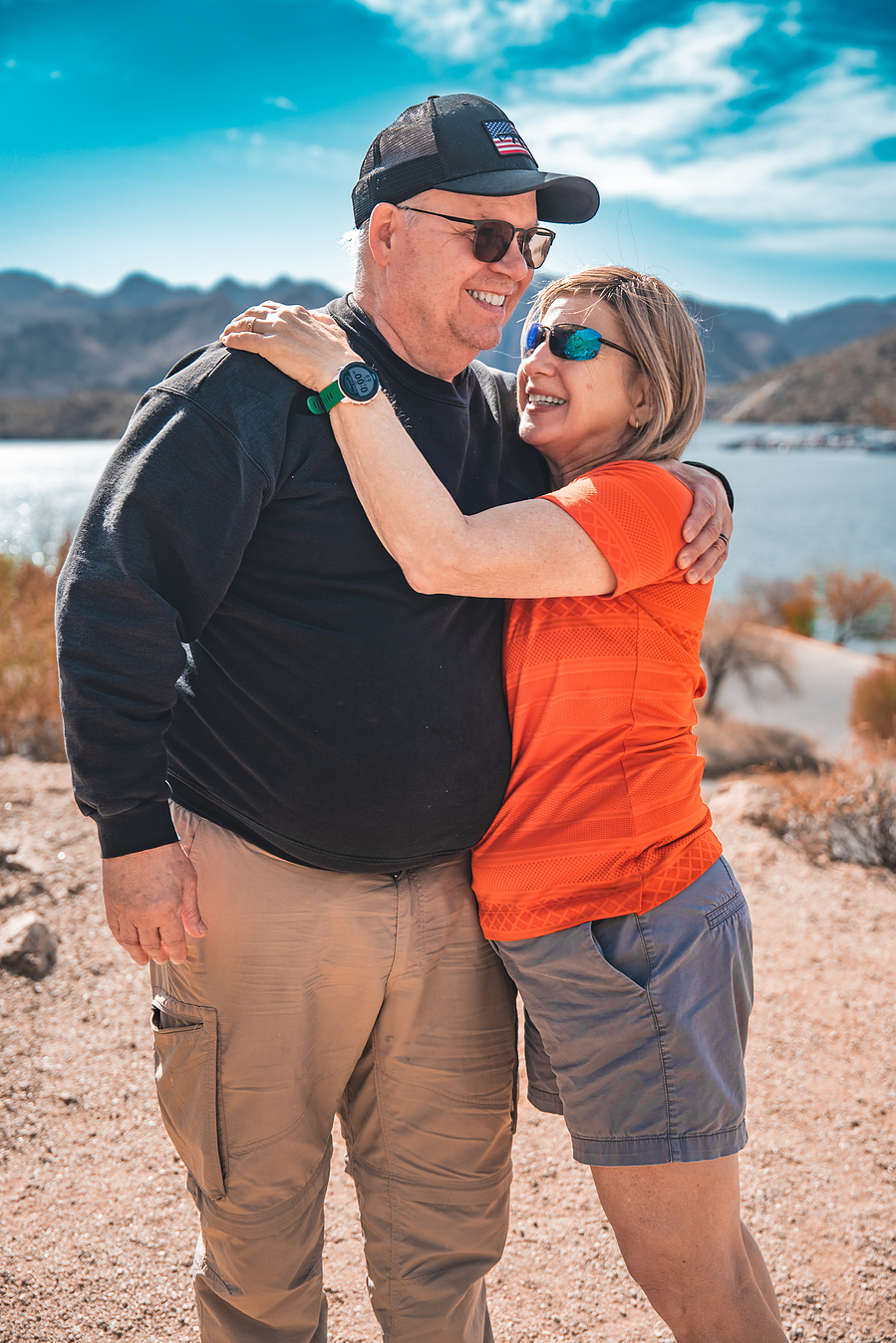 Playful moment between a couple laughing in front of Arizona desert cliffs and lake scenery.