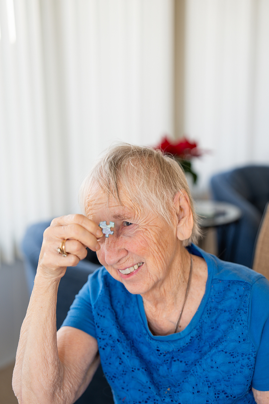 A joyful 90-year-old senior woman holds a puzzle piece with a smile, showcasing active aging and brain wellness through engaging indoor activities.