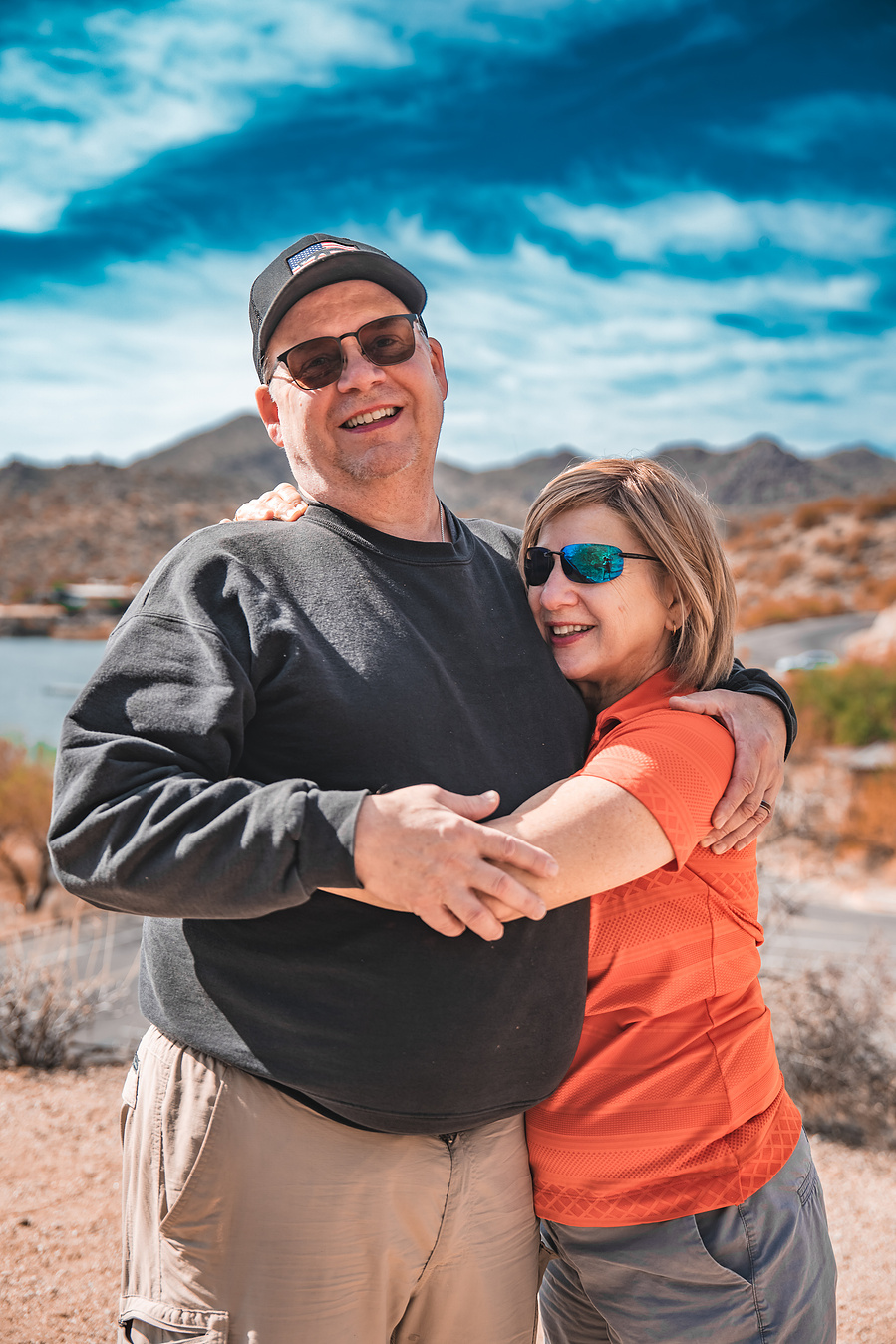Romantic couple hugging on a trail overlooking Saguaro Lake, surrounded by wild desert landscape.
