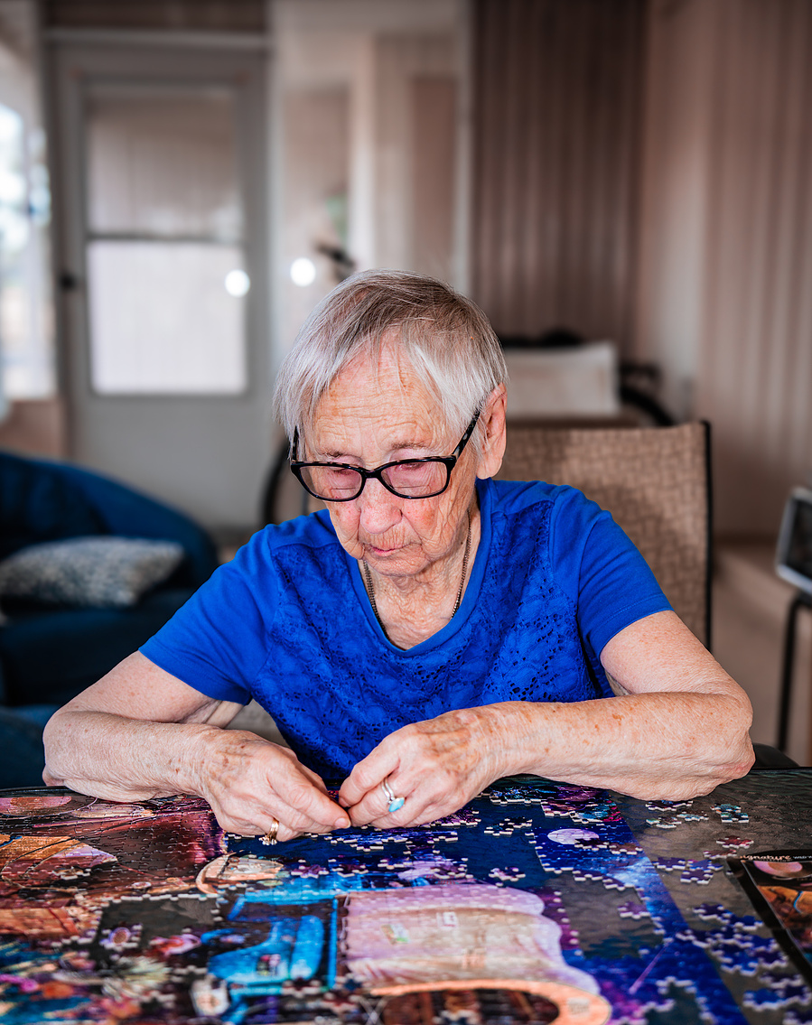 Focused and sharp, this elderly woman concentrates on completing a colorful jigsaw puzzle, promoting cognitive health and senior mental fitness.