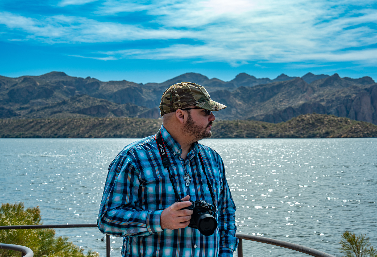 Man standing near Saguaro Lake with mountain reflections and bright desert sun.