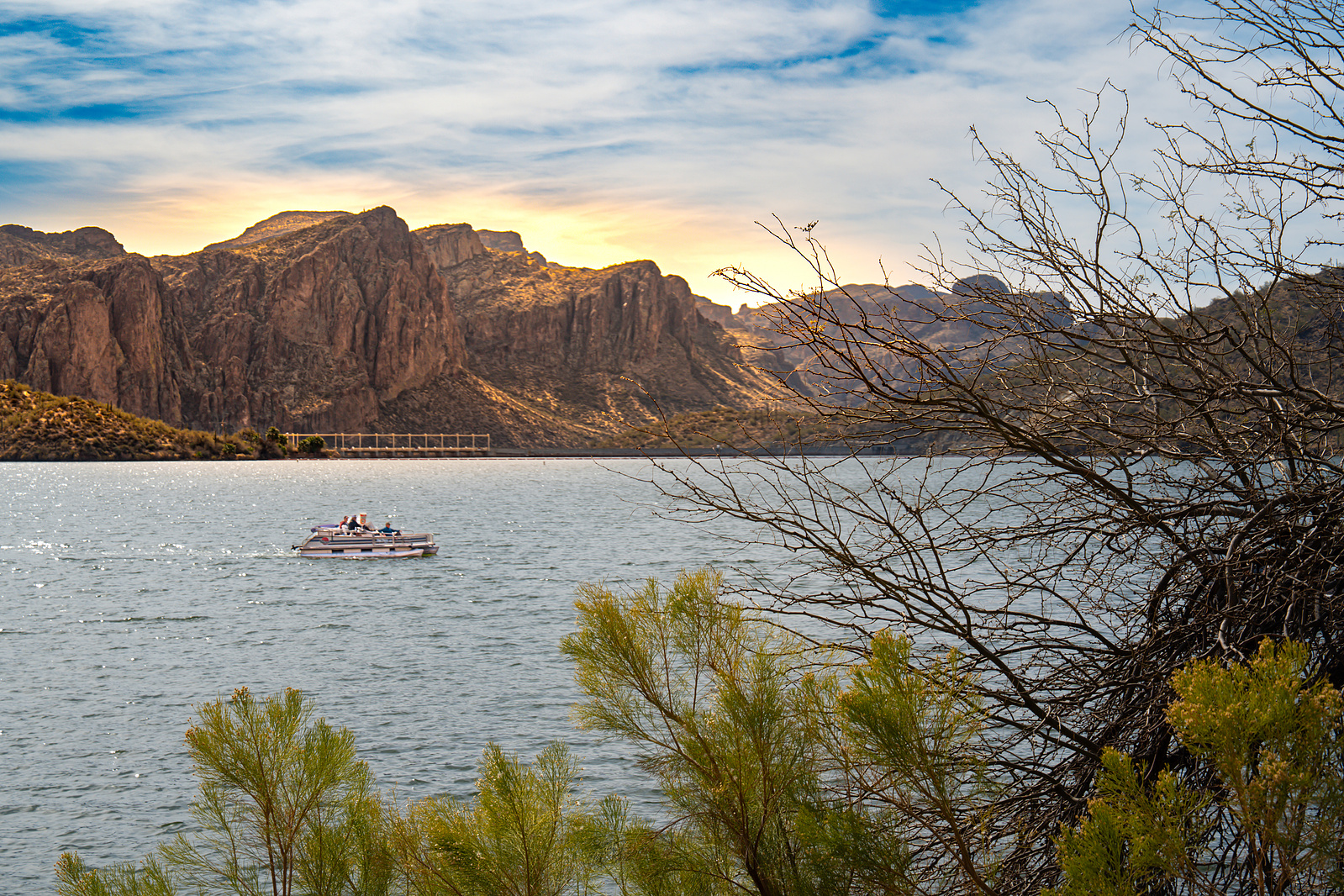 Tour boat on Saguaro Lake surrounded by desert mountains and calm waters during golden hour in Arizona.