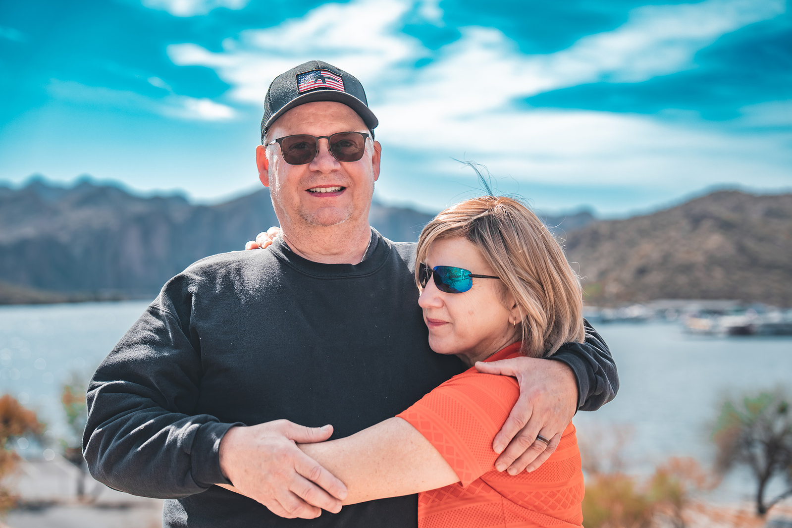 Romantic couple hugging on a trail overlooking Saguaro Lake, surrounded by wild desert landscape.