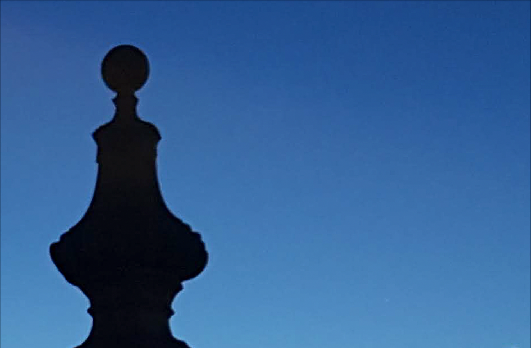 a dusky blue sky, against which is the silhouette of a symmetrical shape (the top of an embellished stone gate) - it looks a little like a pawn in chess.