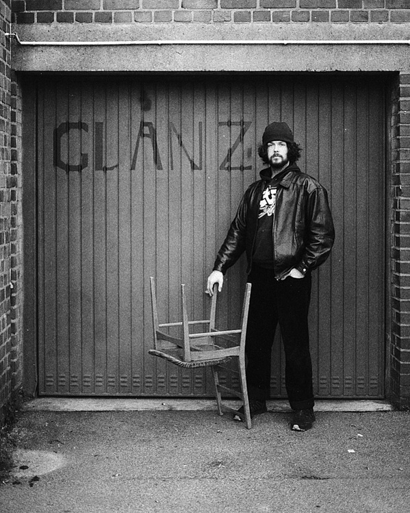 Jonas Glanz, Bielefeld-based photographer, poses in front of a garage with 'GLANZ' written on it. He holds an upside-down chair in his hand, showcasing a unique and creative stance for the camera.

Jonas Glanz, Fotograf aus Bielefeld