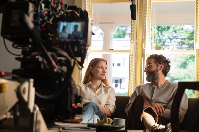 Un homme et une femme assis sur un canapé pendant un tournage. On y voit une caméra en train de filmer