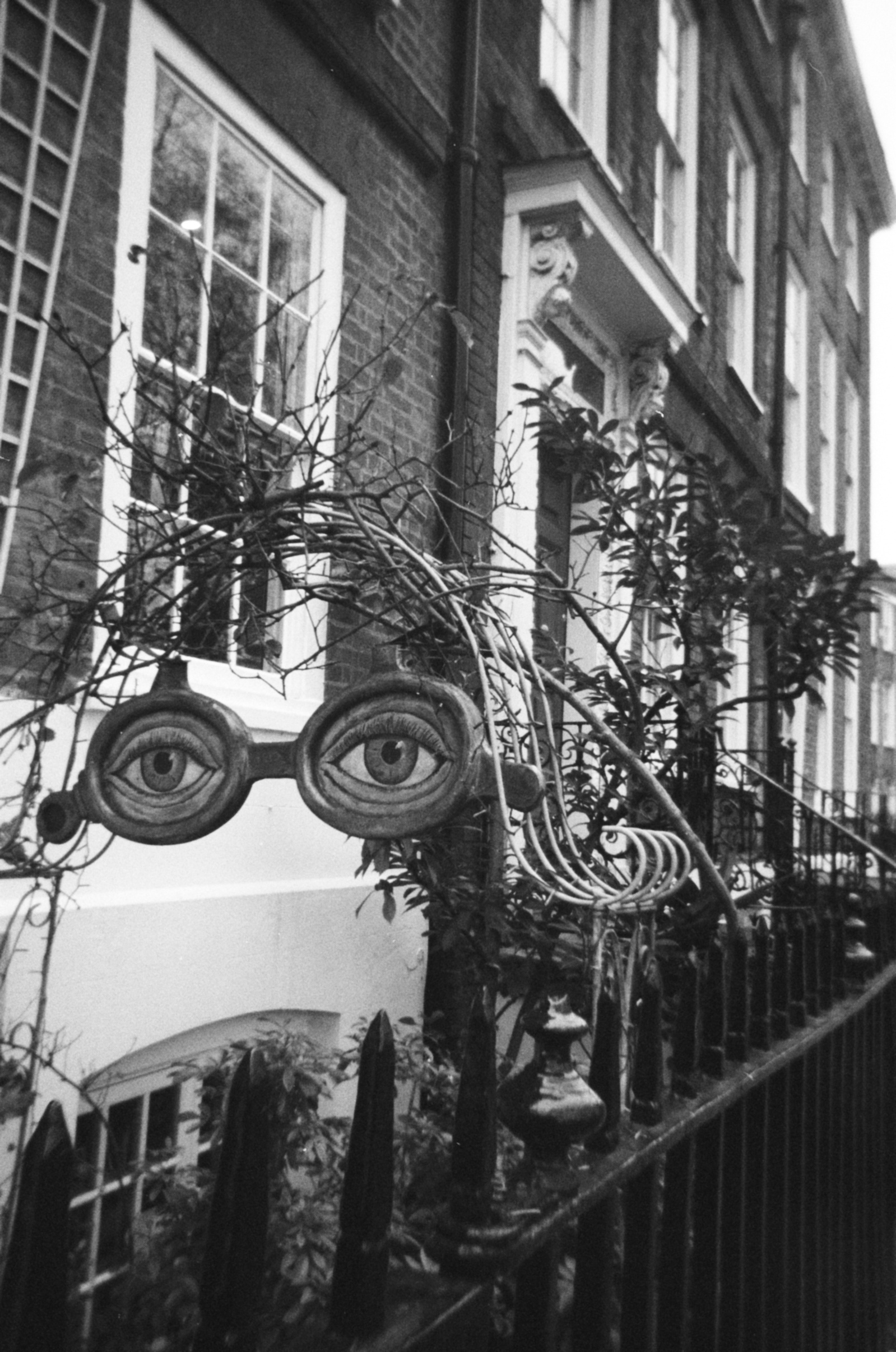 A sculpture of eyes hangs from an arched gate in front of a town house
