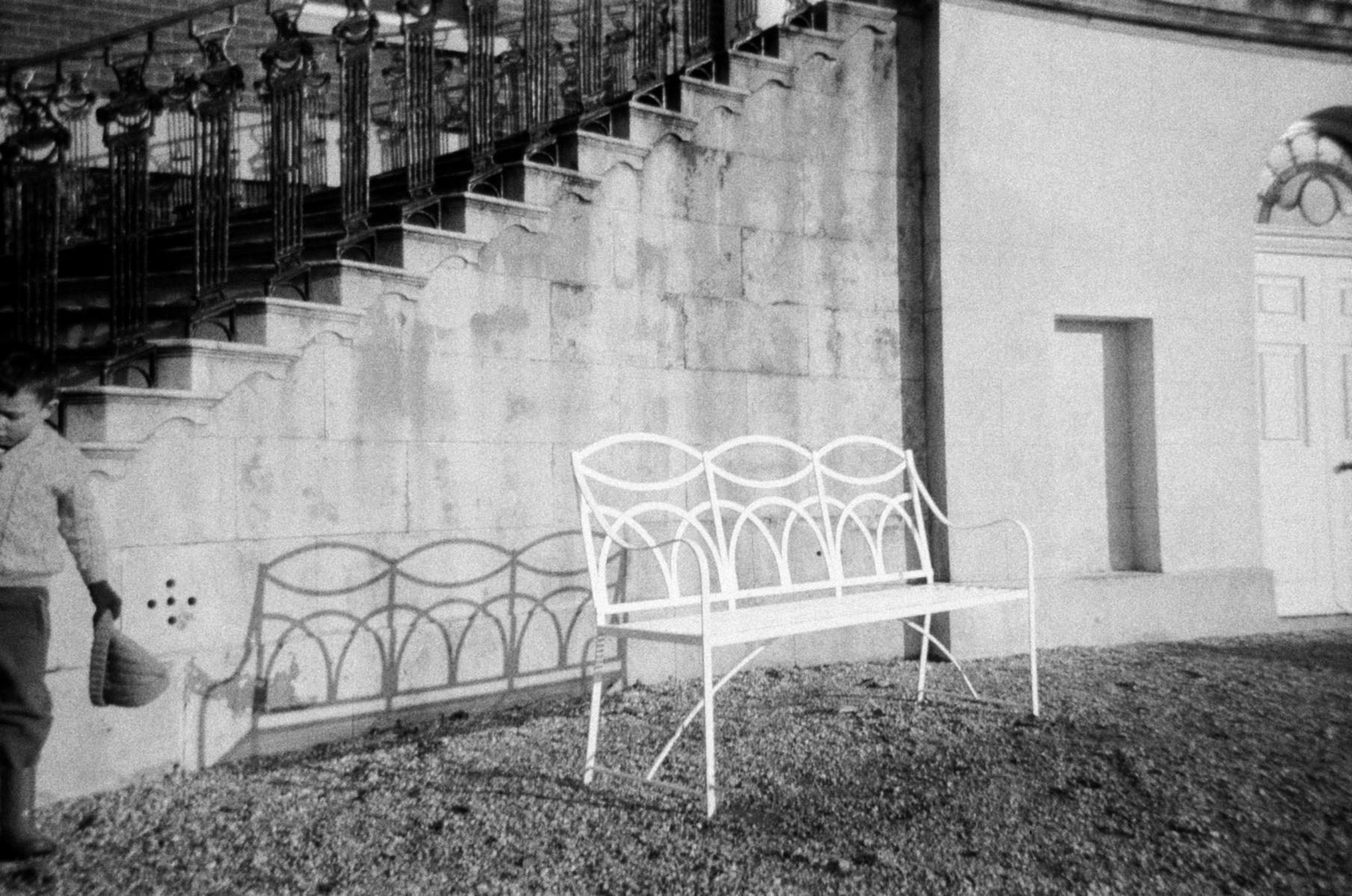 A white metal bench sits on a beach while a small child plays off camera