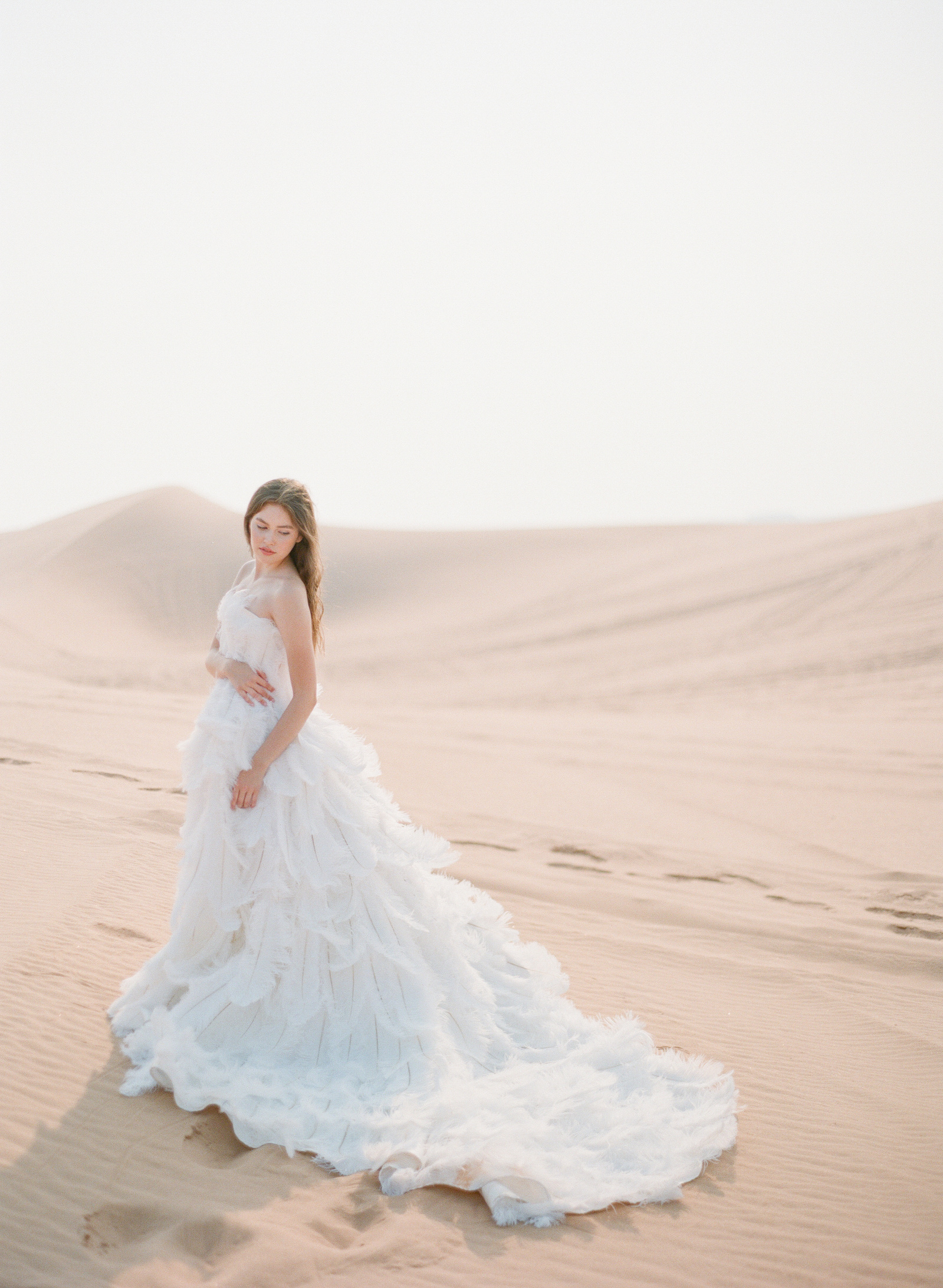 bride wearing a white ostrich feather wedding gown on the sand dunes in the desert