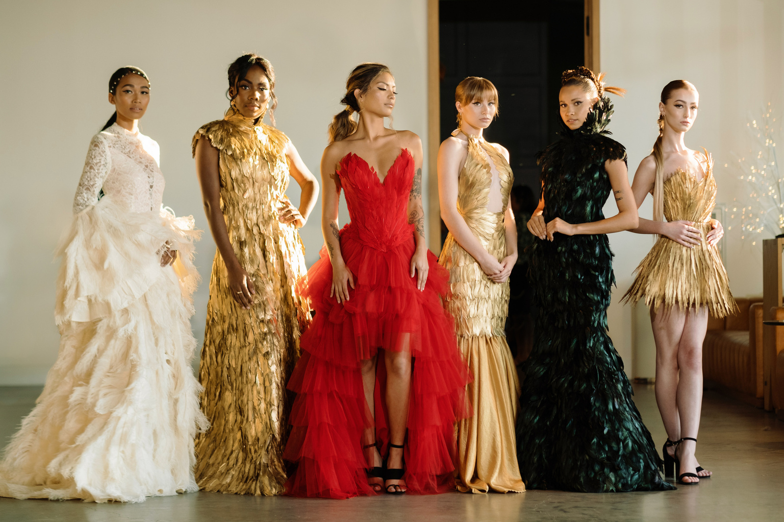 Models wearing couture feather dresses in white, gold, red, and black