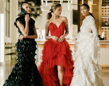 three models wearing red and black and white couture feather dresses at a cocktail bar