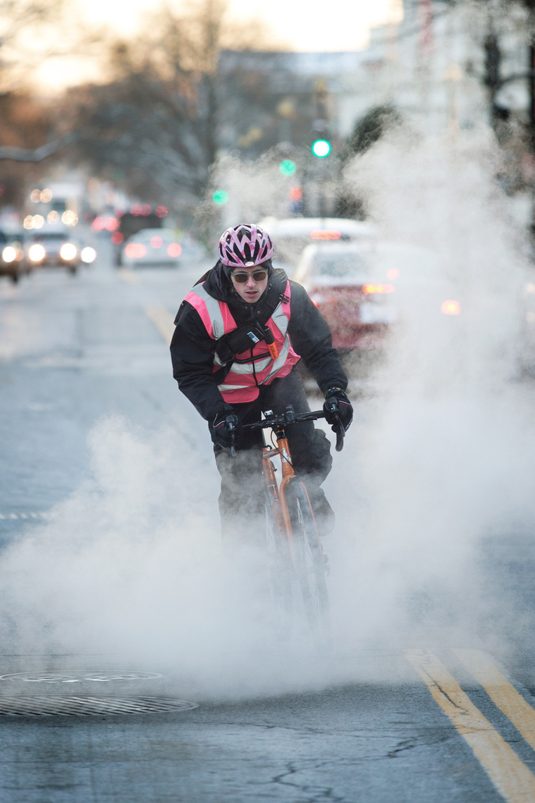 A bike messenger rides through steam as it rises through a man hole in Washington, DC.
