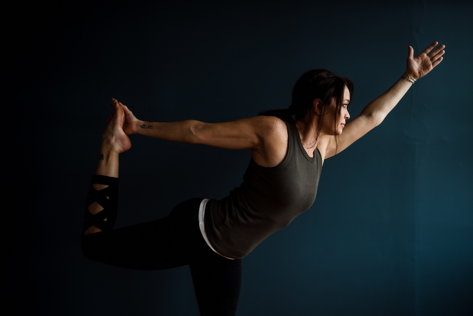 Yoga teacher Jill Barry in dancer pose against a blue wall in the Norwood photography studio of Boston yoga photographer Korri Leigh Photography