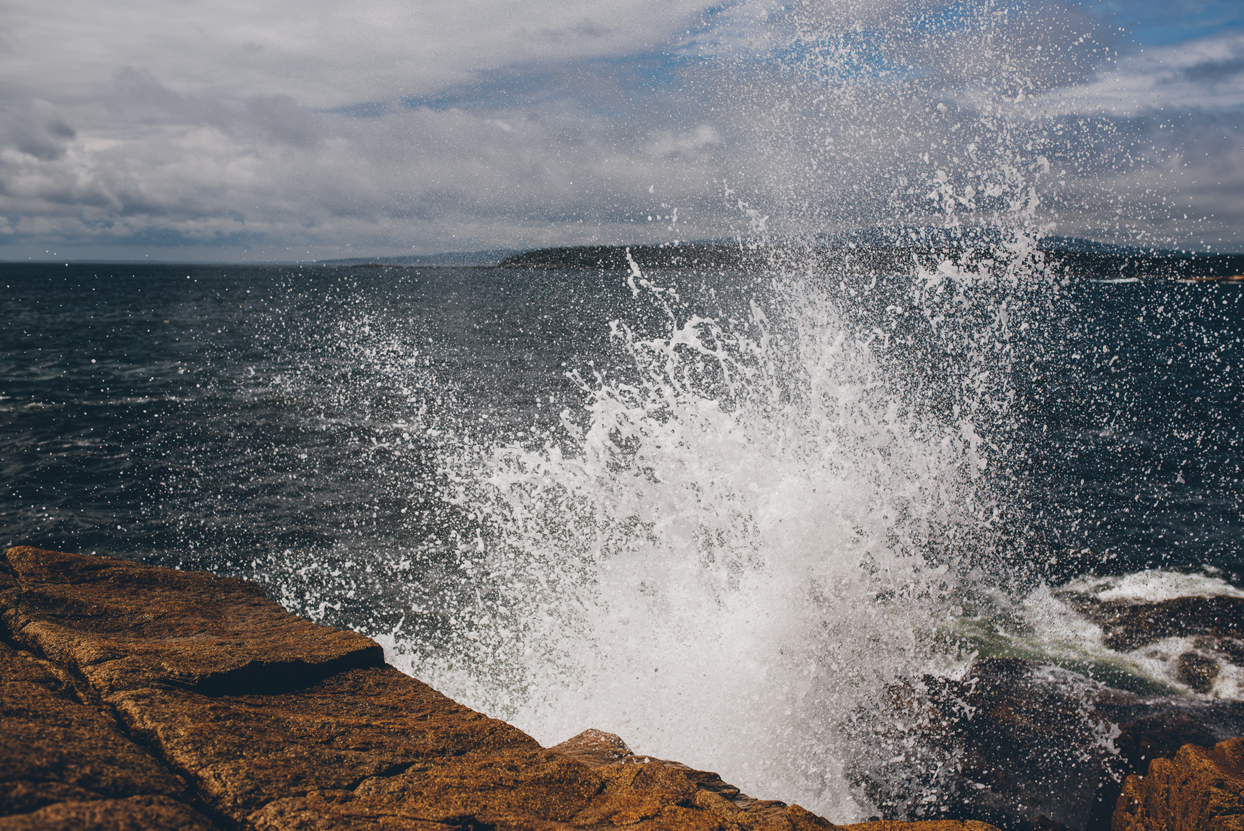 A wave crashes along the rocky Maine coast in Acadia National Park taken by Boston landscape photographer Korri Leigh Crowley