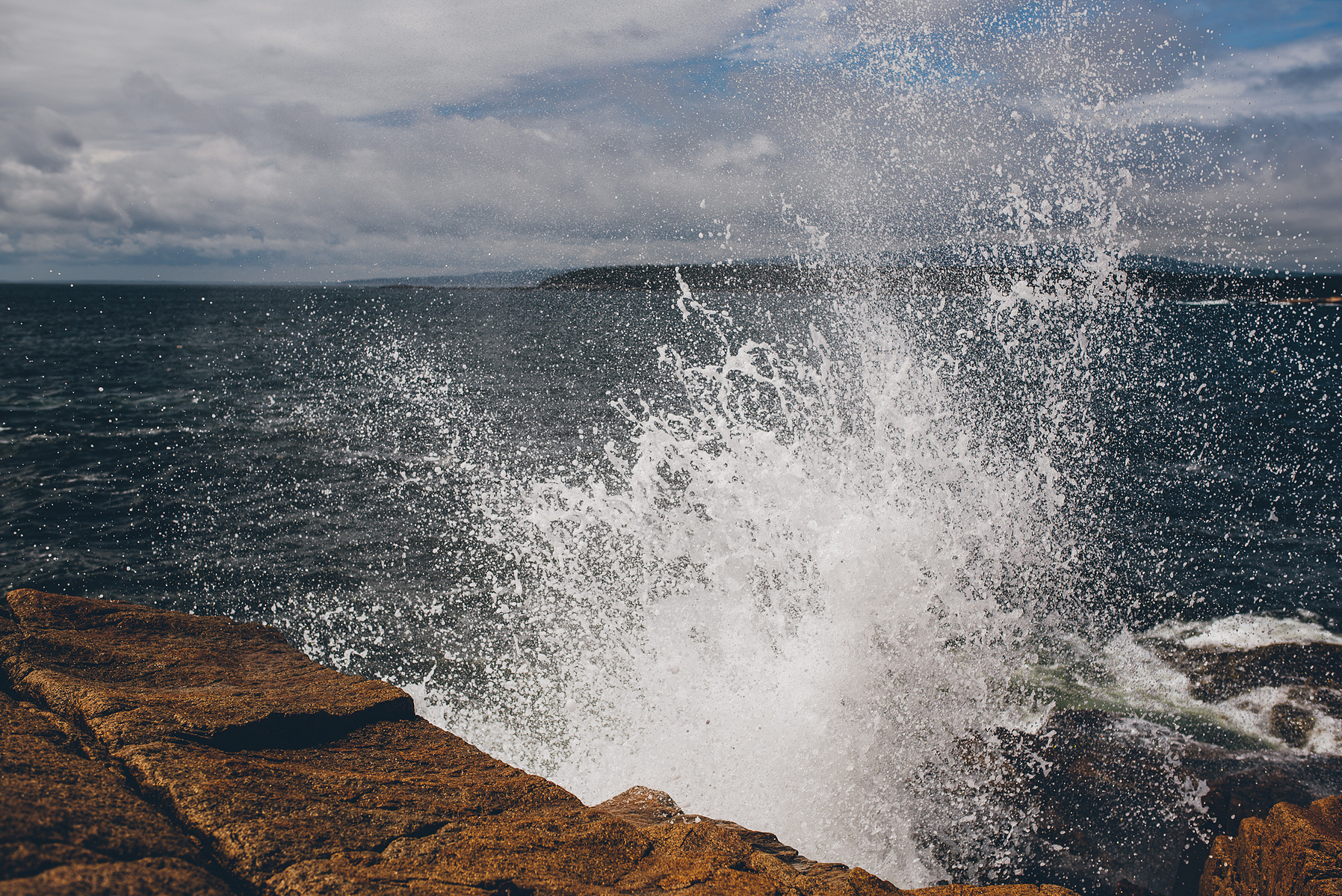 A wave crashes along the rocky Maine coast in Acadia National Park taken by Boston landscape photographer Korri Leigh Crowley