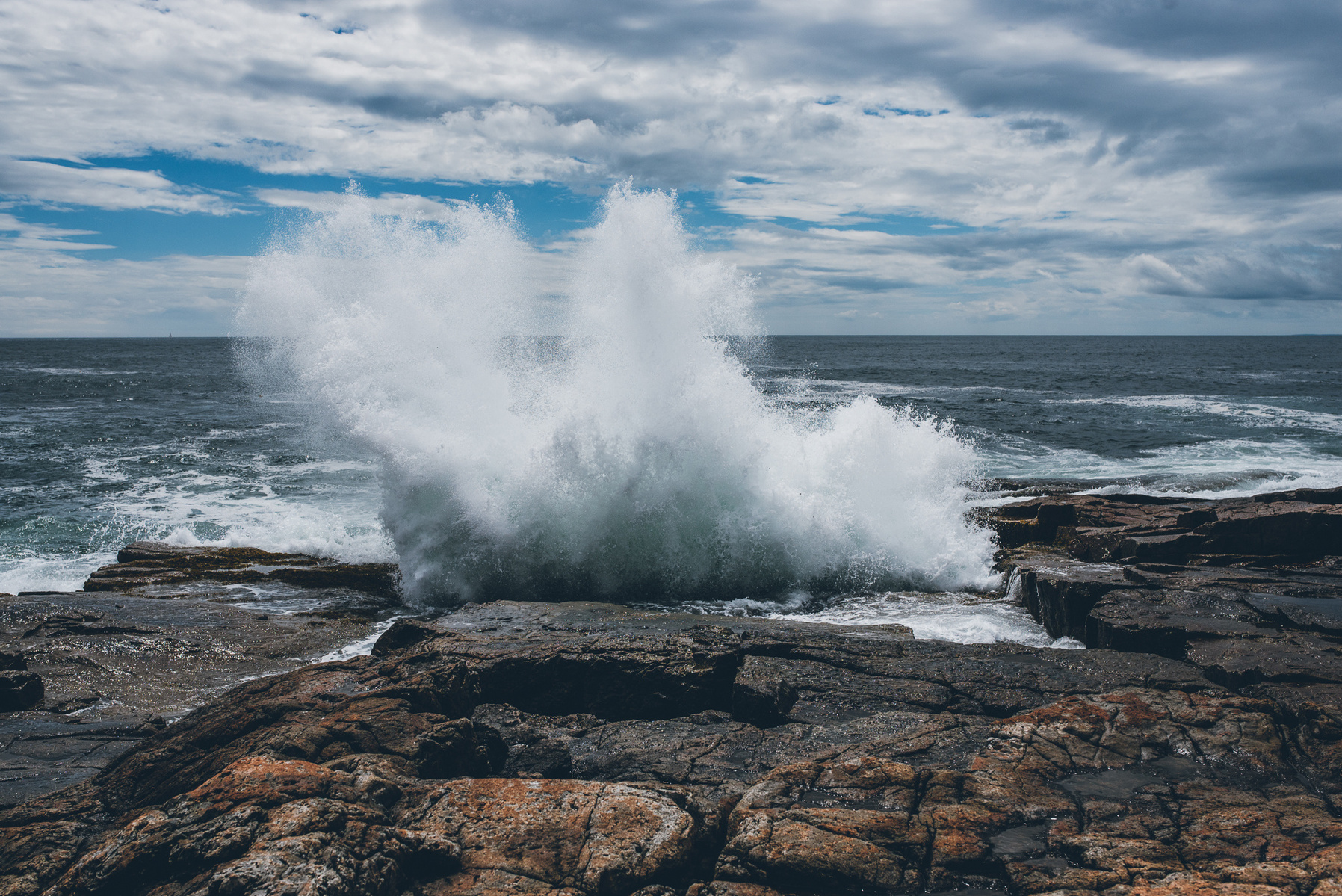 A wave crashes along the rocky Maine coast in Acadia National Park taken by Boston landscape photographer Korri Leigh Crowley