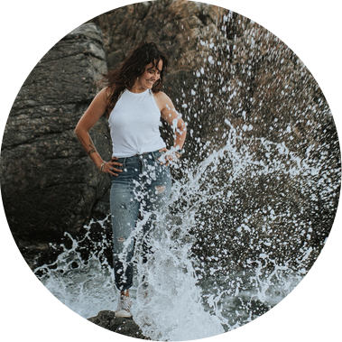 West Roxbury photographer Korri Leigh Crowley stands on a rock in the ocean while a wave crashes over her