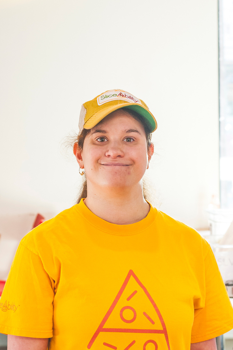 A young woman in a yellow shirt and baseball cap smiles for the camera. 