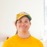 A young woman in a yellow shirt and baseball cap smiles for the camera. 