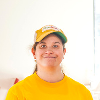 A young woman in a yellow shirt and baseball cap smiles for the camera. 