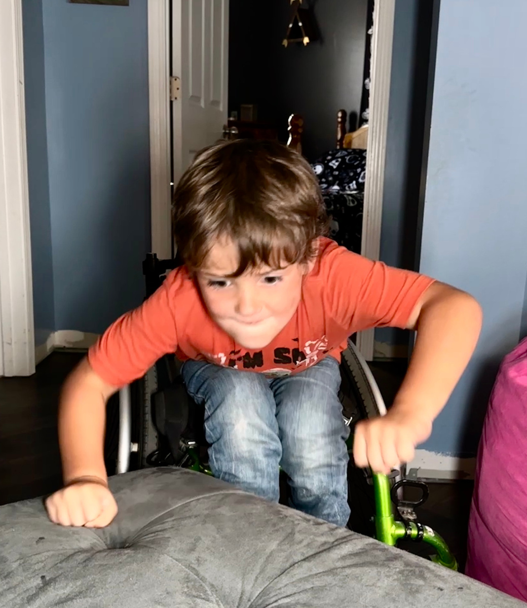 A young boy jumps out of his wheelchair onto a bed. 