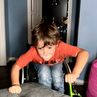 A young boy jumps out of his wheelchair onto a bed. 