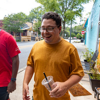 Two men walk next to each other down a sunny street.