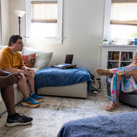Three adults sit in a sun filled room and talk. 