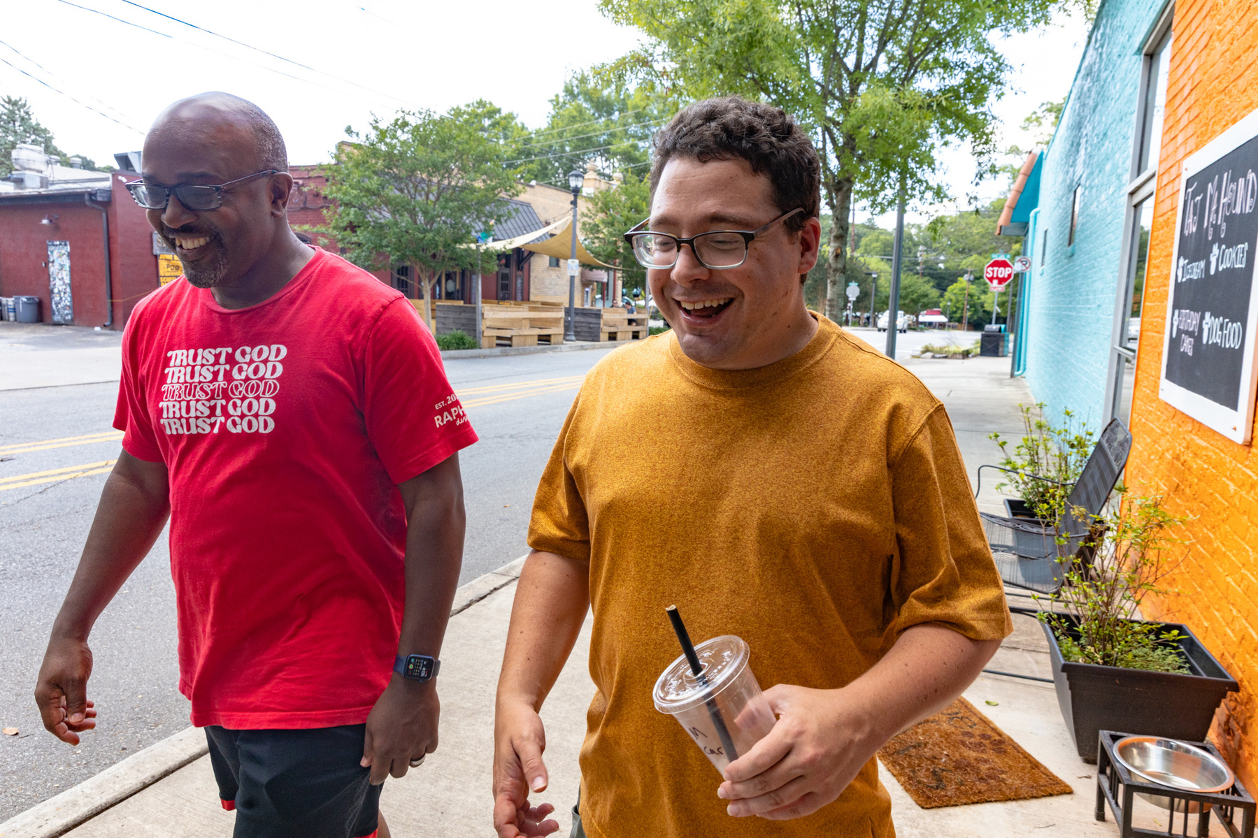 Two men walk next to each other down a sunny street.