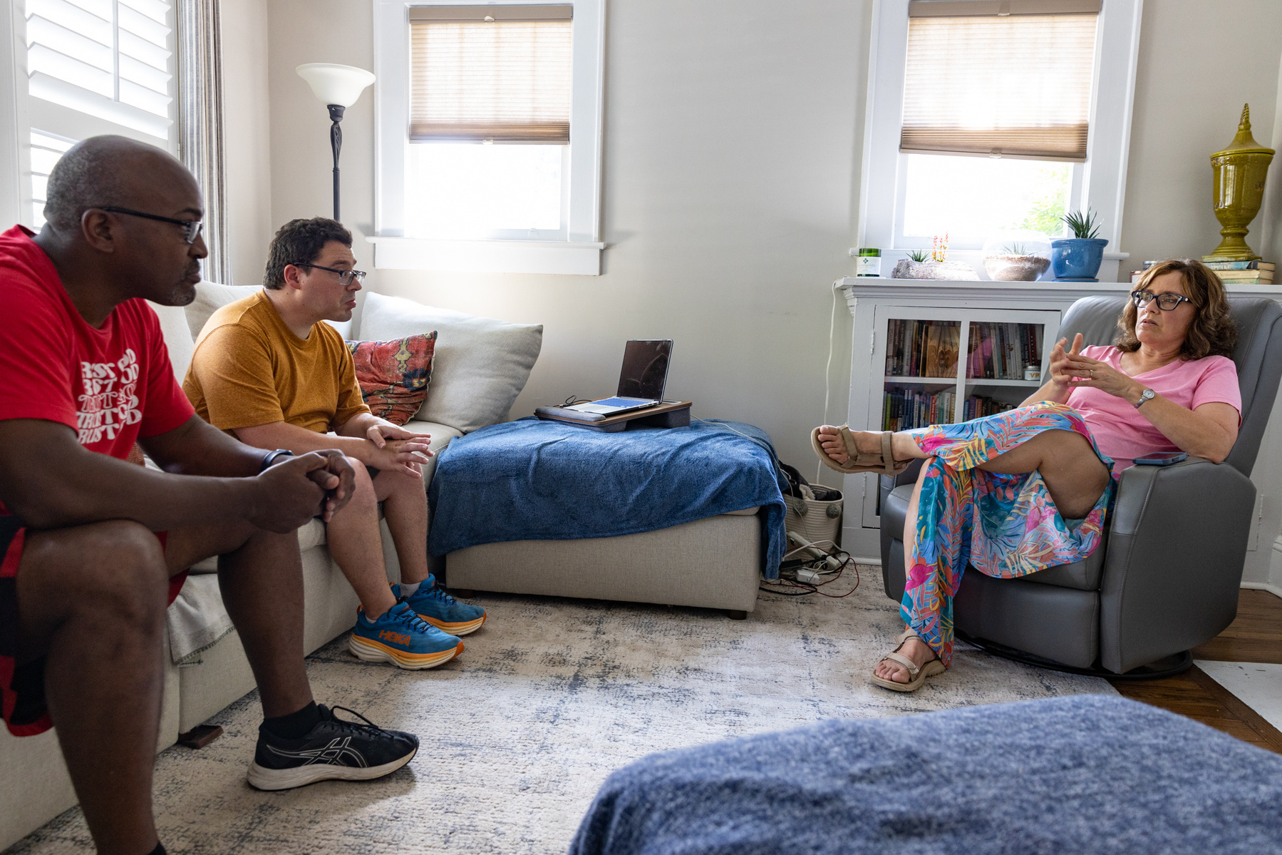 Three adults sit in a sun filled room and talk. 