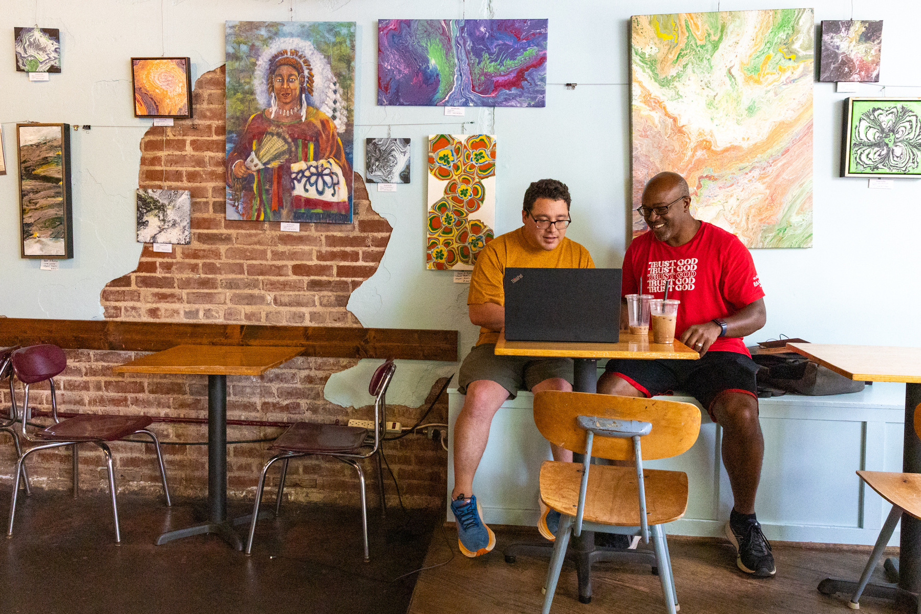 Two men sit next to each other and work on a laptop computer. 