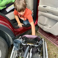 A young boy transfers out of a car into his wheelchair.
