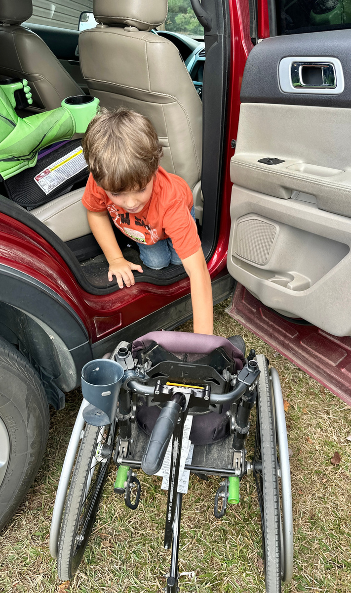 A young boy transfers out of a car into his wheelchair.