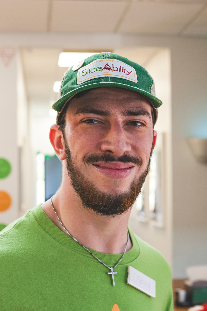 A bearded young man wears a green t-shirt and baseball cap.
