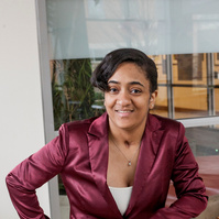 Tavia is an African American college student wearing a rose blazer and jeans. 